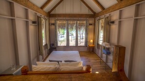 Une chambre avec un grand lit, des poutres en bois, une fenêtre avec des rideaux et une petite table avec des serviettes.