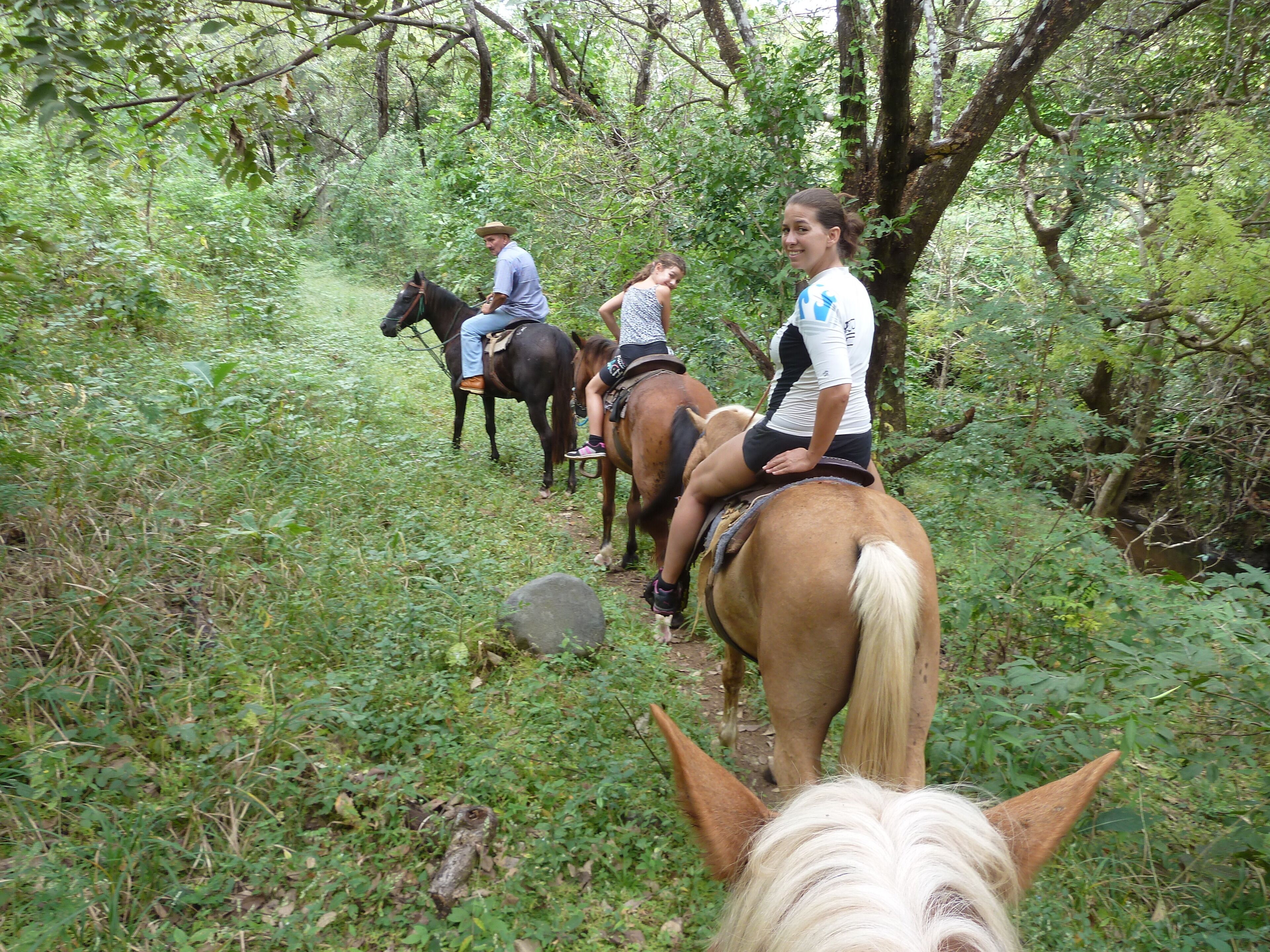 Un grupo de personas montando a caballo por un sendero estrecho rodeado de vegetación densa.