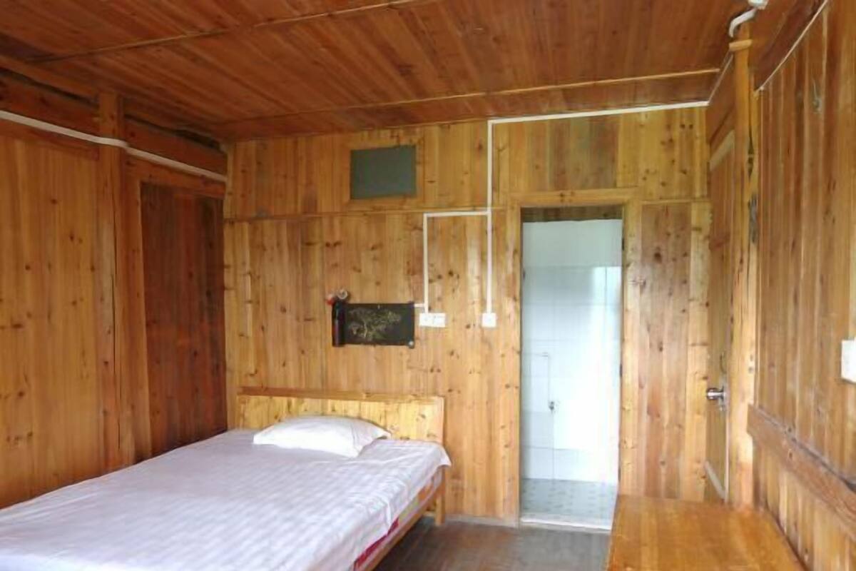 A wooden room with a bed, a small window, and a door leading to another room.