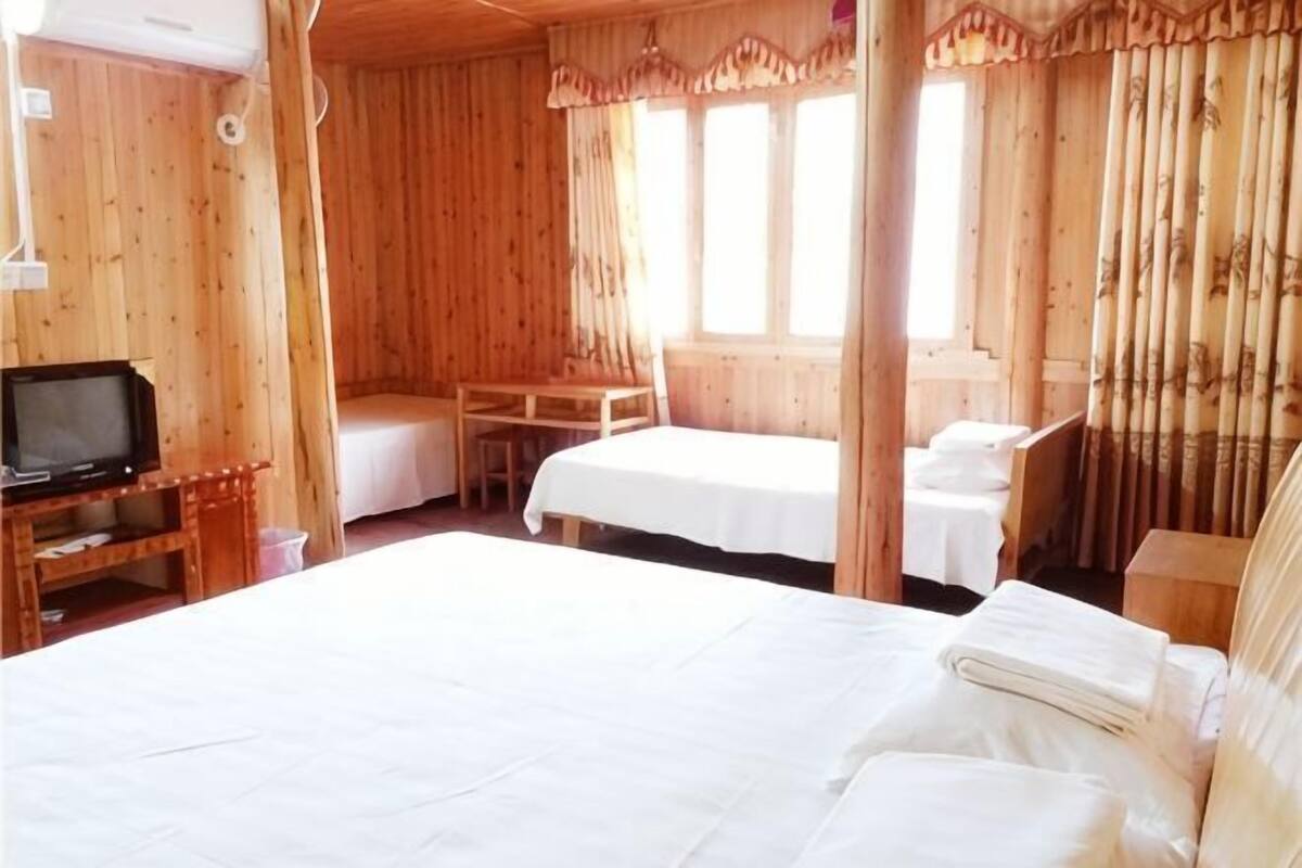 A wooden room with a bed, a desk with a TV, and two single beds.