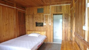 Quarto de madeira com uma cama, uma porta que dá para outro espaço e uma pequena janela.