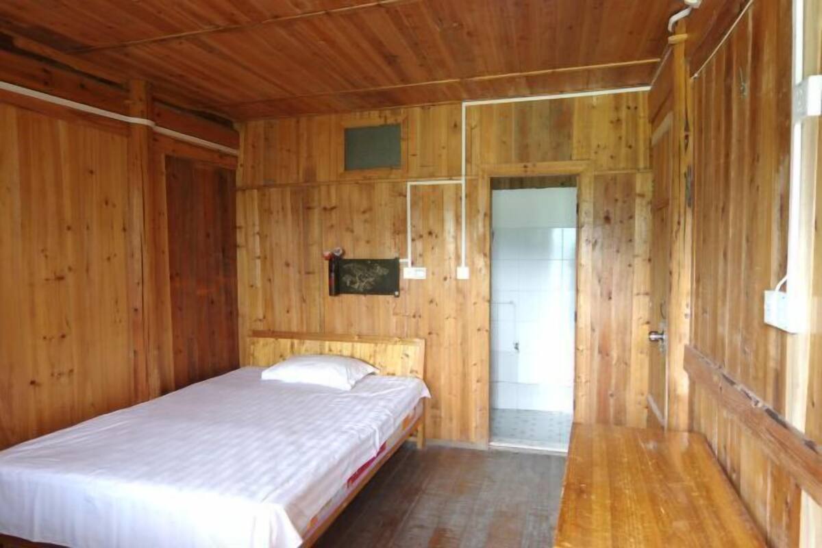 A wooden room with a single bed, a door leading to another room, and a small window.