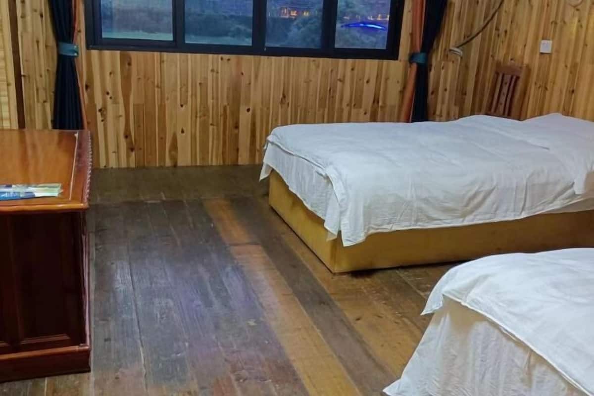 A room with two beds, wooden walls, a wooden desk, and a window with a view.