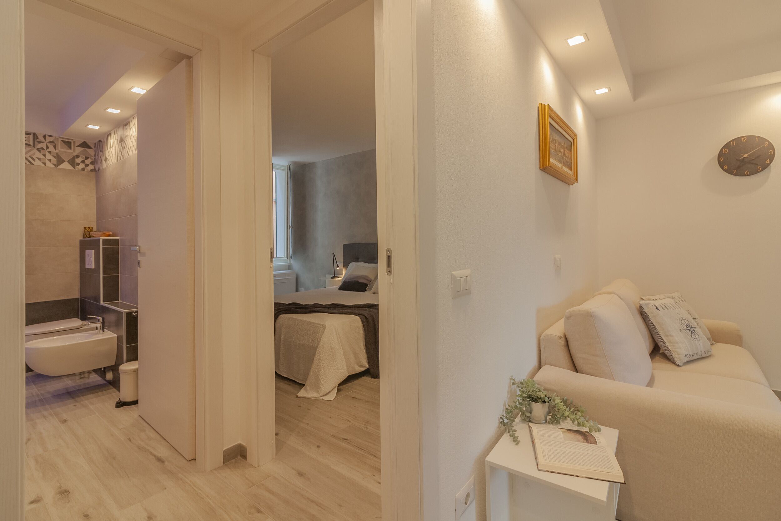 Une salle de bain moderne avec une baignoire, des toilettes et une douche. On y trouve un lit recouvert d’une courtepointe blanche et une table de chevet agrémentée d’une plante.