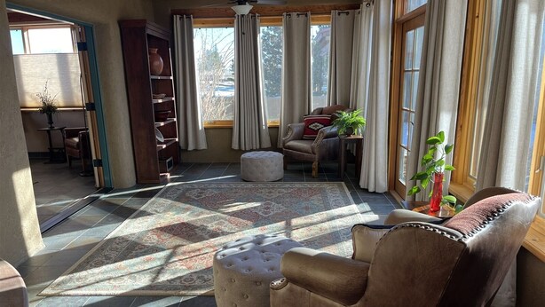 Un salon spacieux avec une grande fenêtre, un tapis à motifs, un fauteuil en cuir et un plafond en bois.