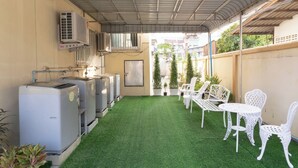 A covered outdoor area with artificial grass, white outdoor furniture, and air conditioning units.