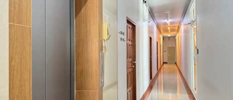 Corridoio di un albergo con una porta in legno, un telefono e una targa con i numeri delle camere.
