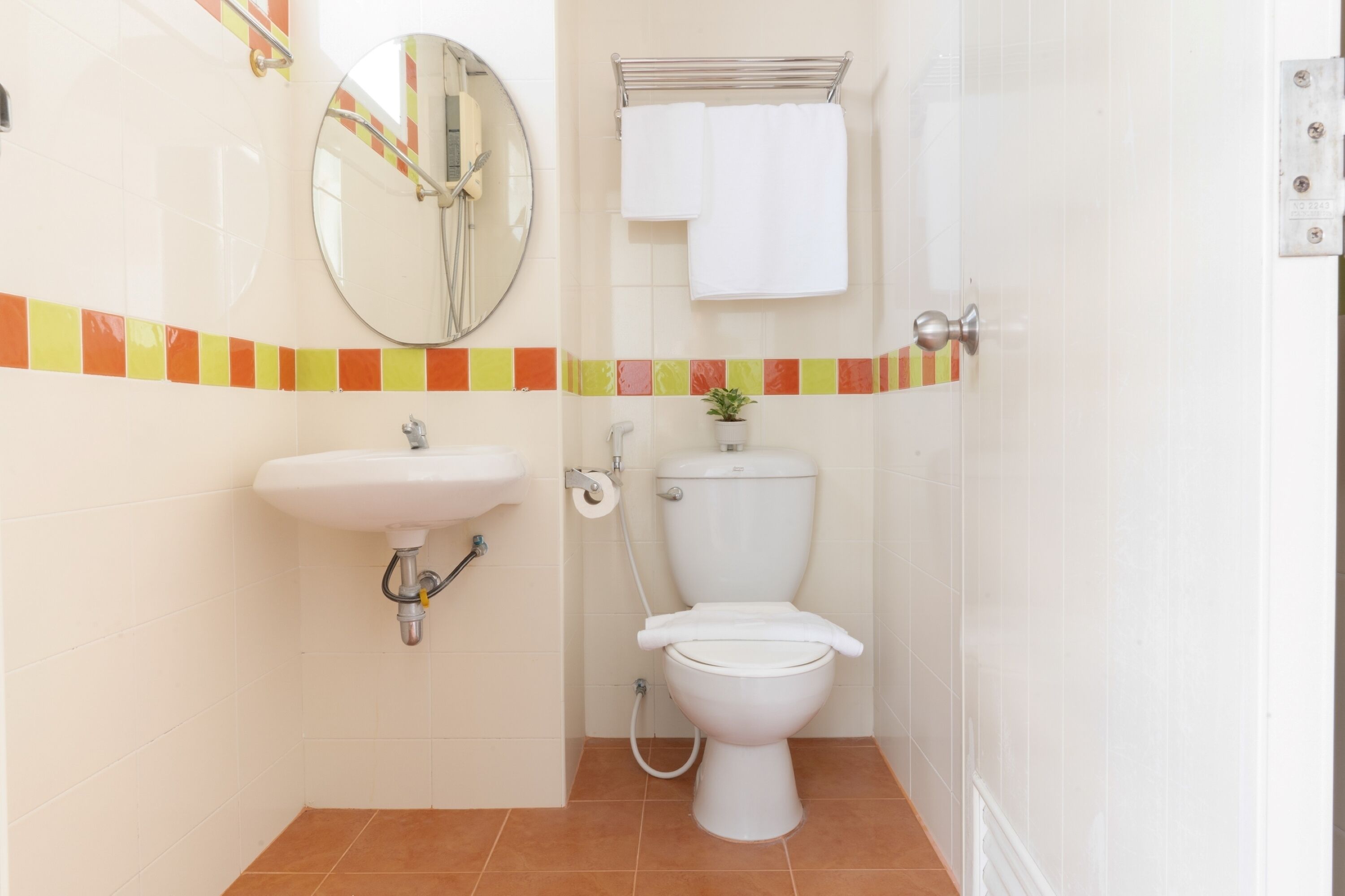 A bathroom with a white sink, toilet, and a mirror. There is a towel rack with two towels and a small potted plant on the counter.