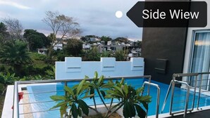 A side view of a modern building with a rooftop pool, surrounded by greenery and overlooking a residential area. - ISLAND RESIDENCE Plaisance - Mauritius - Villa with Private Pool (Island residence,Plaine Magnien)