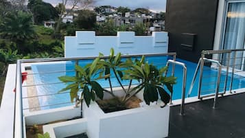 Une vue latérale d’un bâtiment moderne doté d’une piscine sur le toit, entouré de verdure et donnant sur un quartier résidentiel.