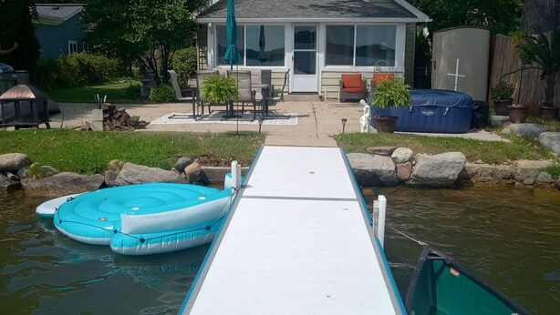 A house with a dock leading to a small boat, a grill, and outdoor furniture. - Lakeside Retreat with Massage Chair (Lapeer)