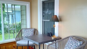 A room with a wooden ceiling, a table with two chairs, a window with a view of greenery, and a lamp on a side table. - Lakeside Retreat with Massage Chair (Lapeer)