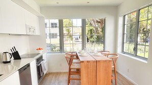 Una cucina moderna con mobili bianchi, un tavolo da pranzo in legno e ampie finestre che offrono vista all'esterno.