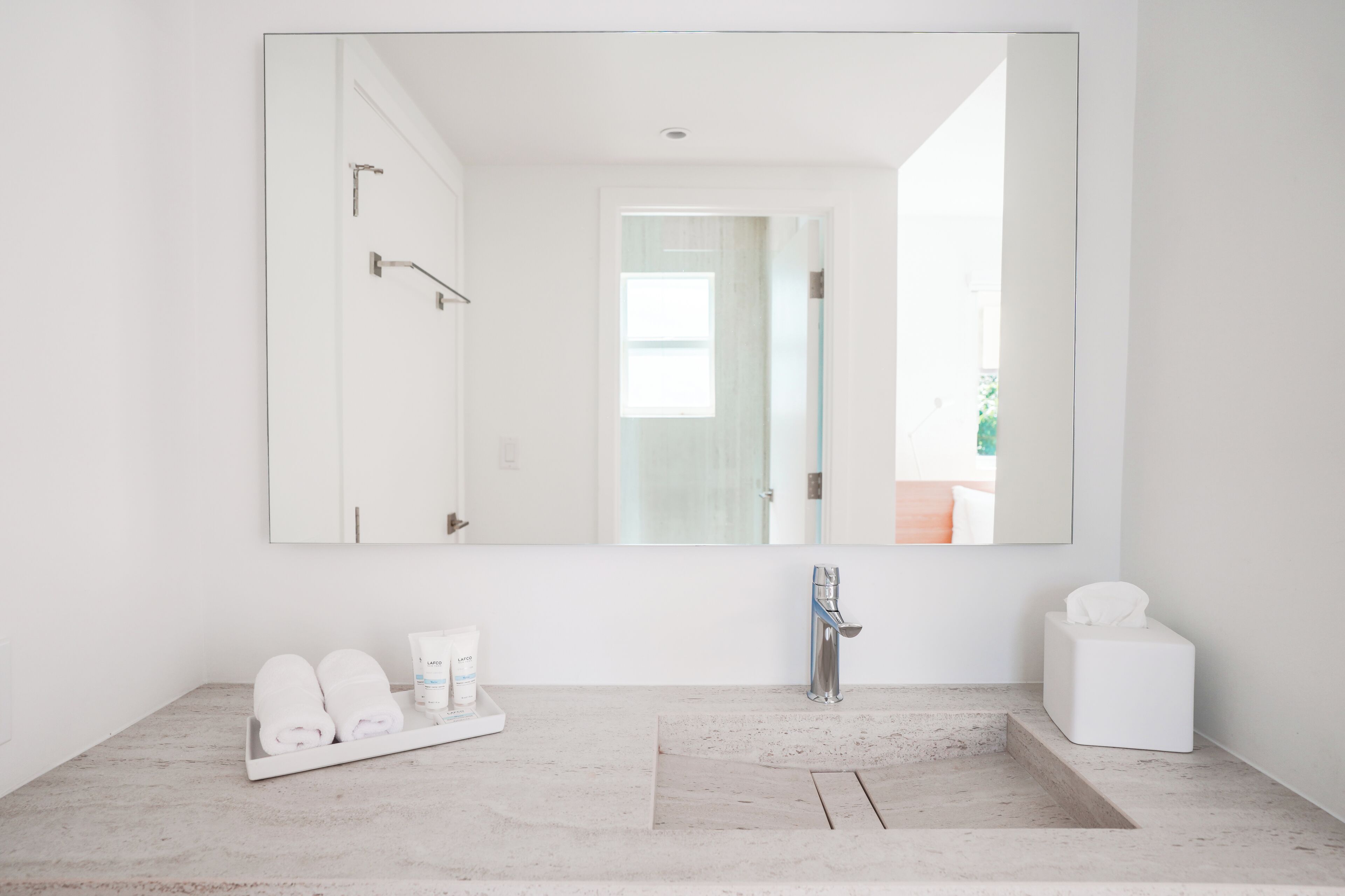 A modern bathroom with a large mirror, a sink, and a shower area. There are towels and toiletries on the counter.