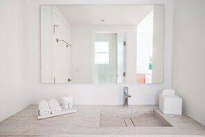 A modern bathroom with a large mirror, a sink, and a shower area. There are towels and toiletries on the counter. - Beach Haus Design District (Miami)