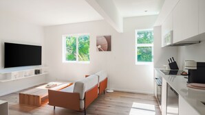 Un soggiorno moderno con una TV a schermo piatto, un divano, un tavolino da caffè e una panca in legno. Sono presenti due finestre che offrono vista sul verde.