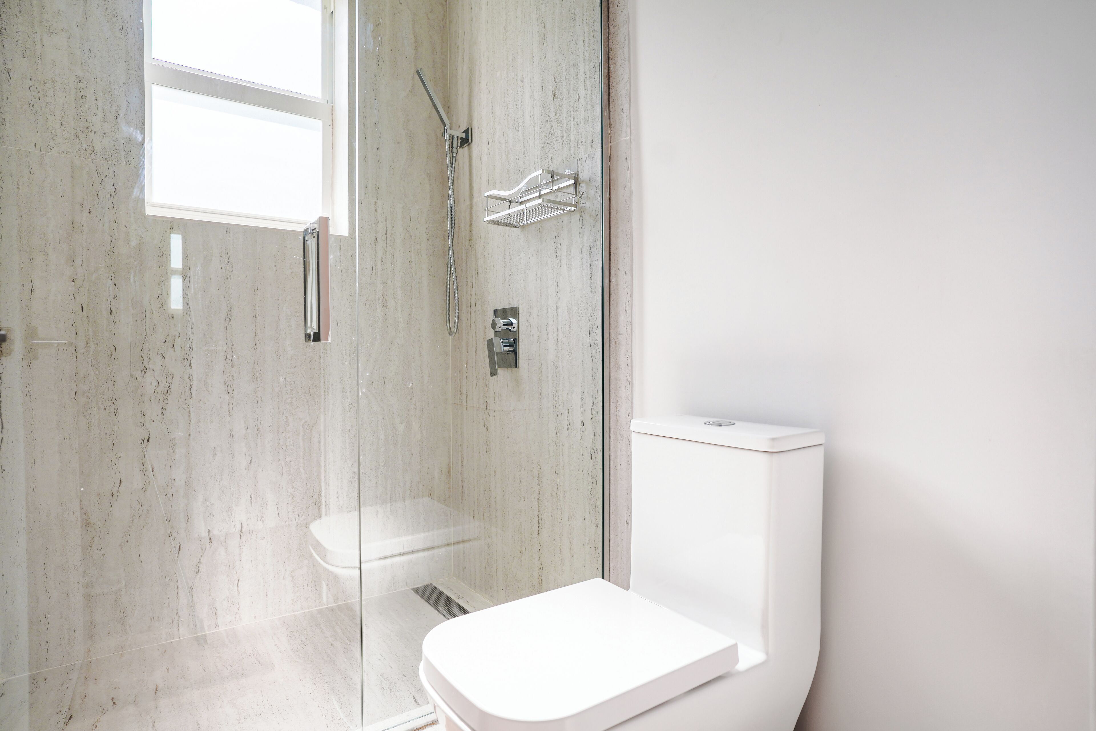 A modern bathroom with a glass-enclosed shower, a white toilet, and a marble wall.