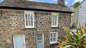 Un bâtiment en pierre doté de nombreuses fenêtres et portes, une enseigne indiquant « Kleingarten Cottage », et un petit escalier menant à l’entrée.