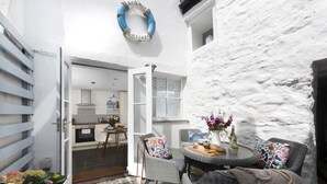 Un espace extérieur accueillant, aménagé avec des meubles en osier, une table dressée et ornée de nourriture, et une guirlande décorative accrochée au mur.