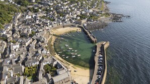 Vue aérienne d’une ville côtière avec un port de plaisance, des bâtiments en pierre et une plage de sable.