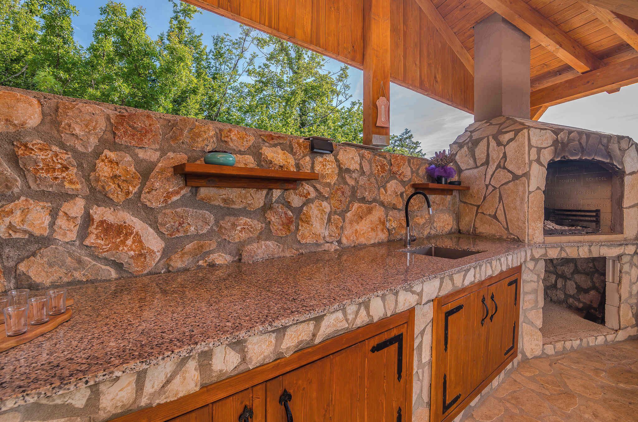 An outdoor kitchen with a stone wall, wooden cabinets, and a built-in pizza oven.