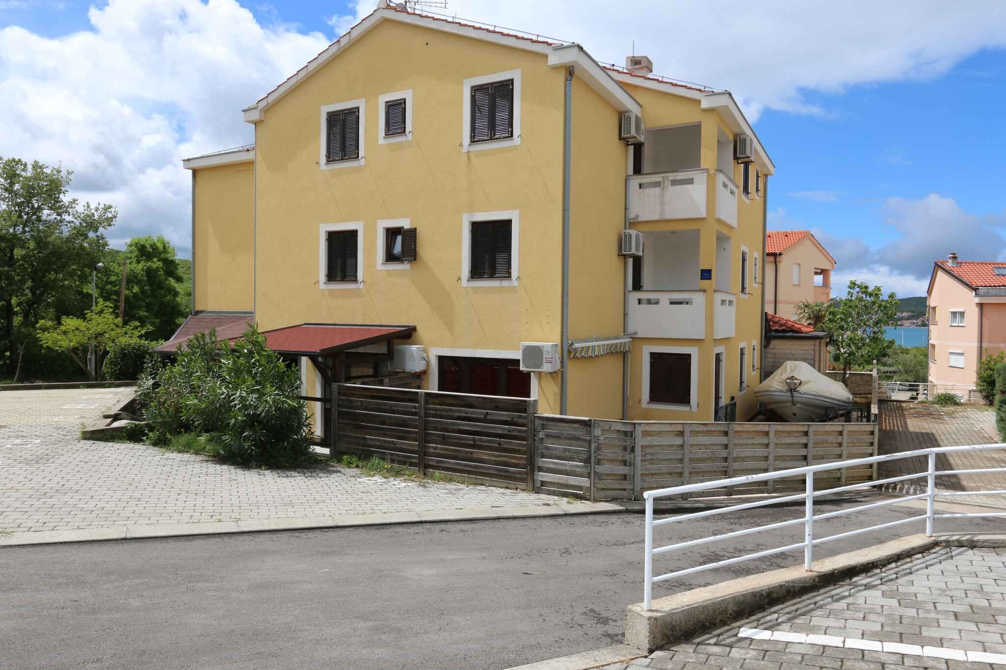 A yellow multi-story building with a red roof, a gated entrance, and a paved driveway.