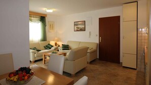 A compact living space with a sofa, a dining table with a fruit bowl, a lamp, and a refrigerator.