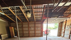 Un grand garage doté d’un sol en béton, de poutres métalliques et d’une porte entrouverte donnant sur l’extérieur.