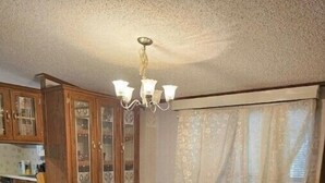 Un coin repas comprenant une table et des chaises, un lustre, des meubles en bois et une fenêtre avec des rideaux.