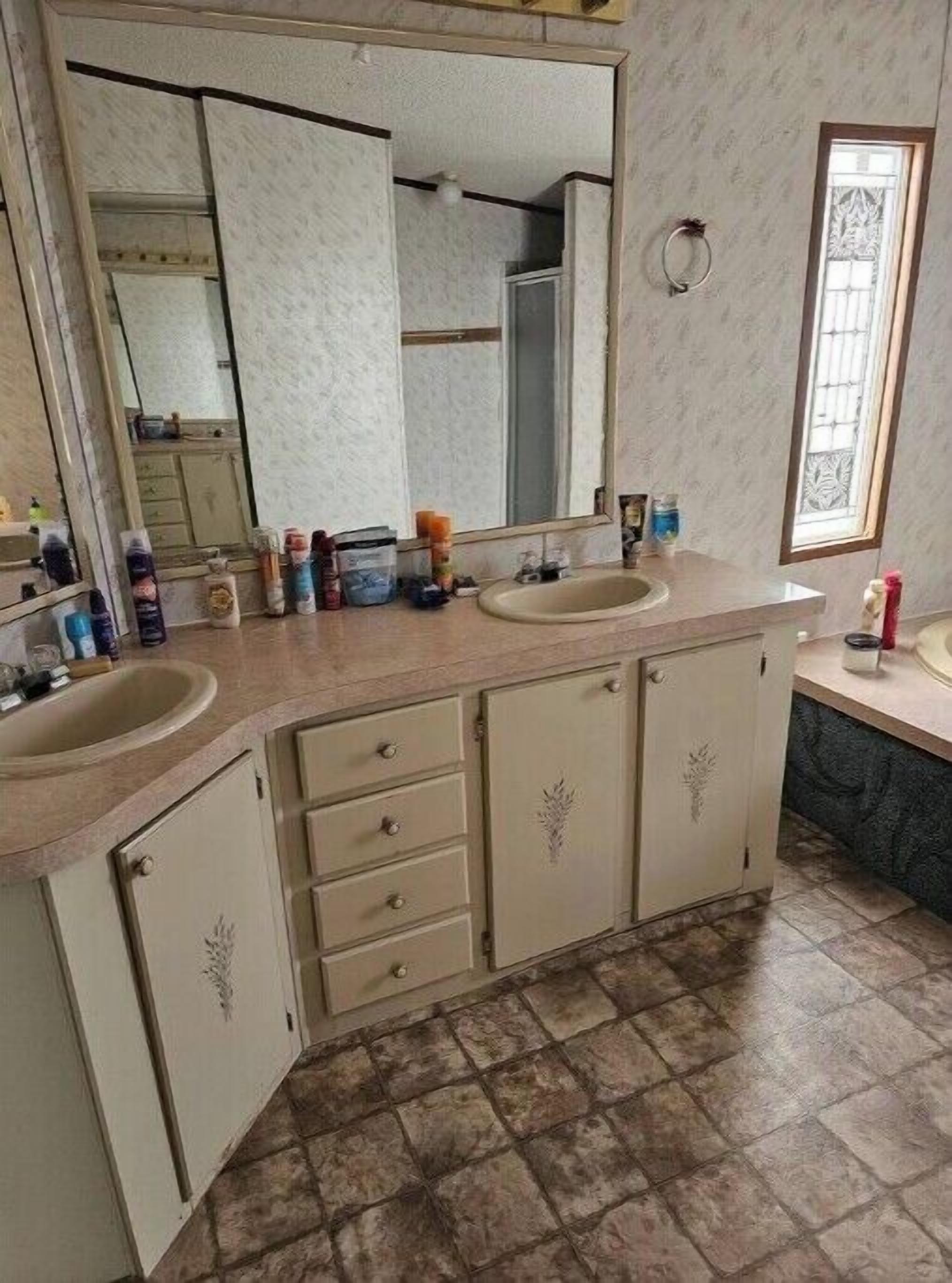 Une salle de bain avec deux lavabos, un grand miroir et une fenêtre avec des barreaux.
