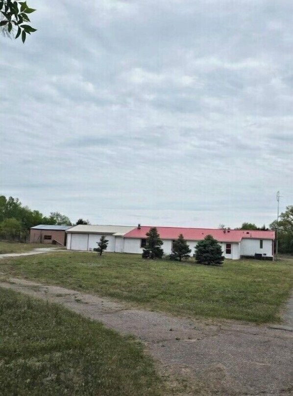 A building with a red roof and white walls, surrounded by a grassy area with a few trees.
