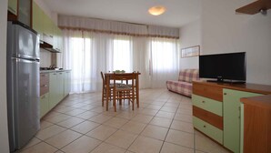 Un espacio habitable compacto con kitchenette, zona de comedor, televisor y sofá.