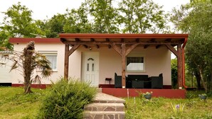 Una casa con porche cubierto, escalones de piedra que llevan a una puerta y mobiliario de exterior.