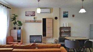 Una sala de estar moderna con sofá, televisión, mesa de comedor, sillas y plantas decorativas.