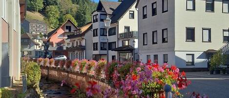 A residential street with houses, a stone wall, and a flower bed.