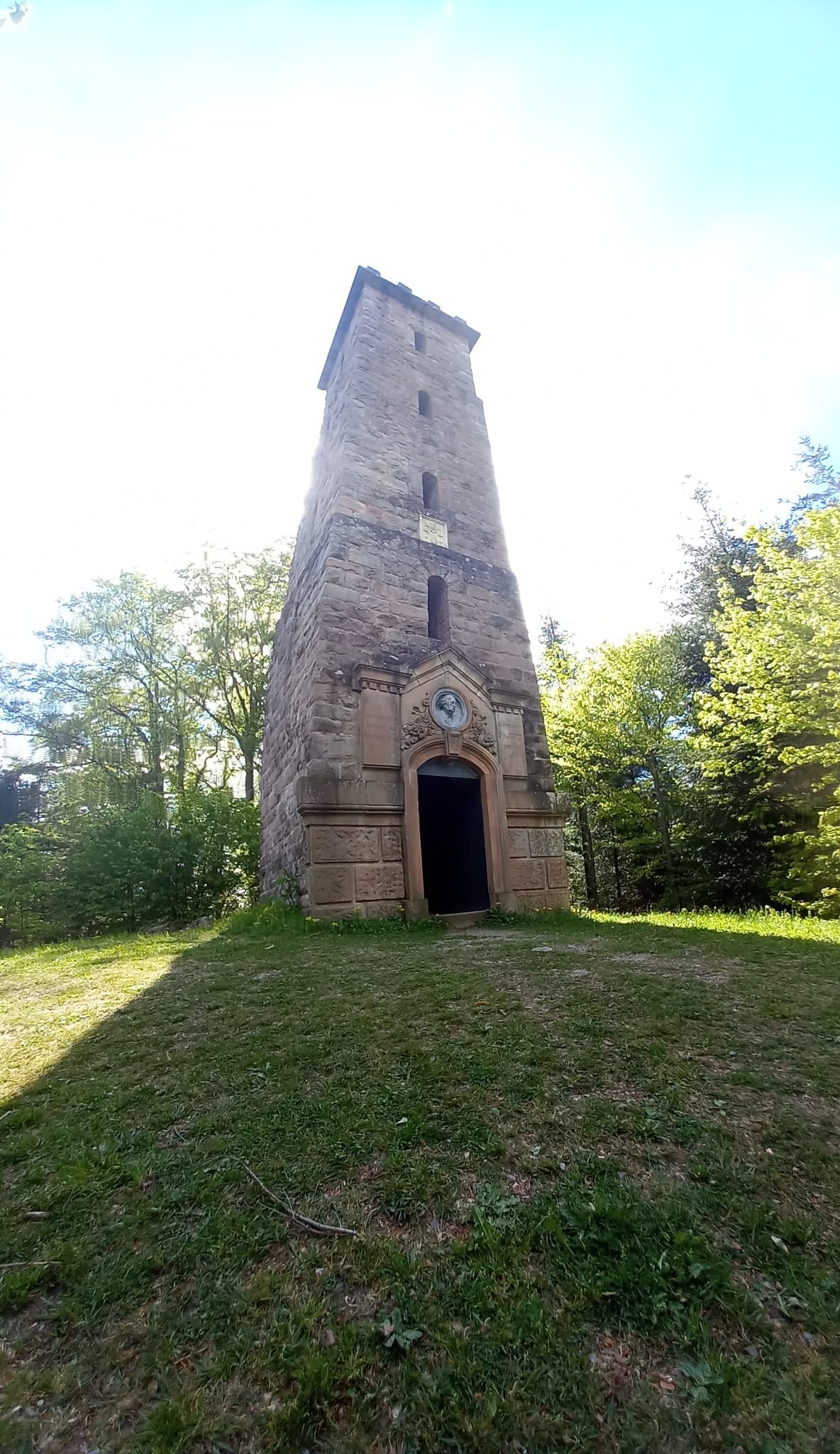 Una torre de piedra con una entrada oscura, rodeada de césped y árboles.