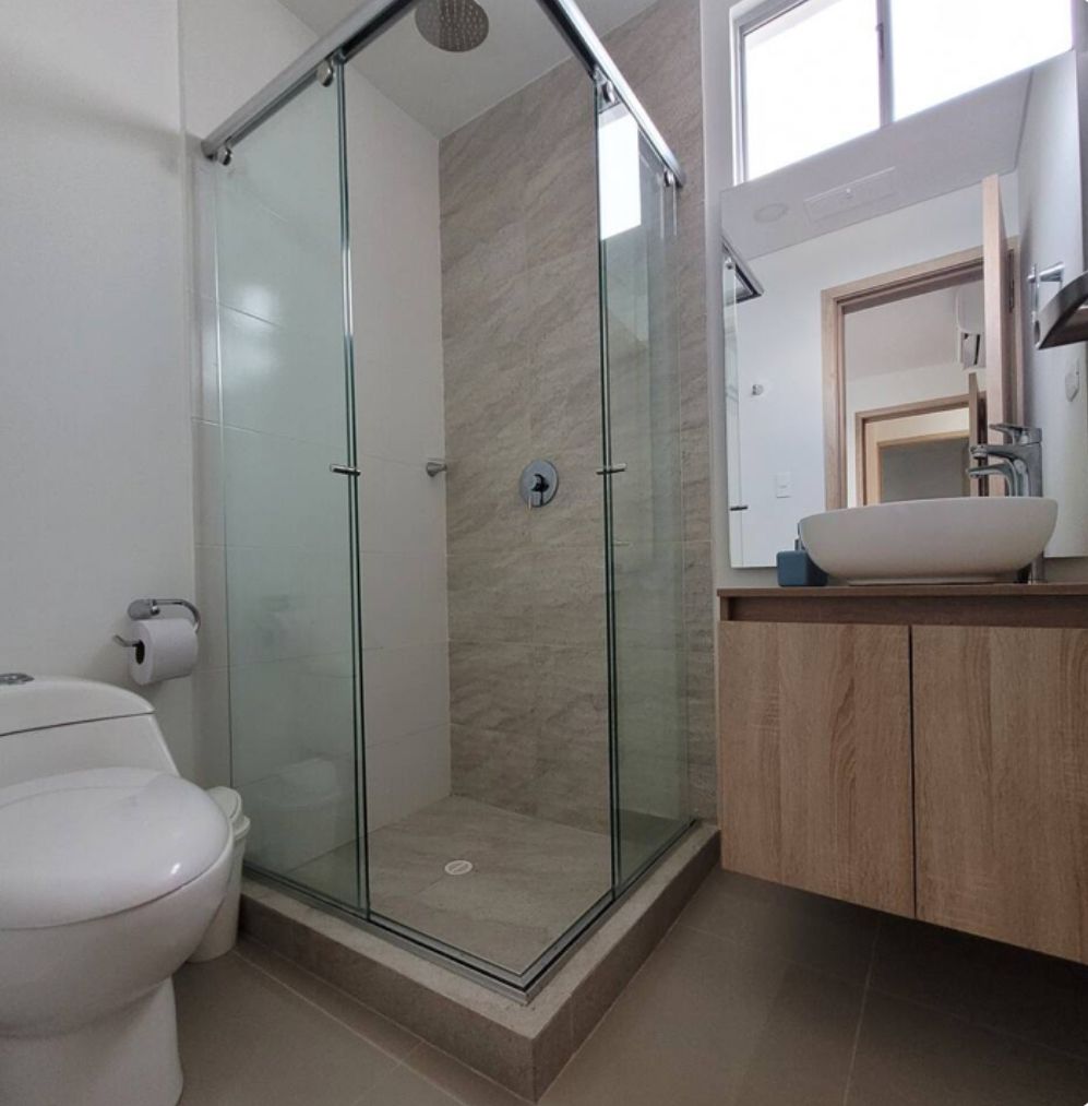 Une salle de bain moderne dotée d’une douche à parois de verre, de toilettes et d’un meuble-lavabo avec un évier et un miroir.