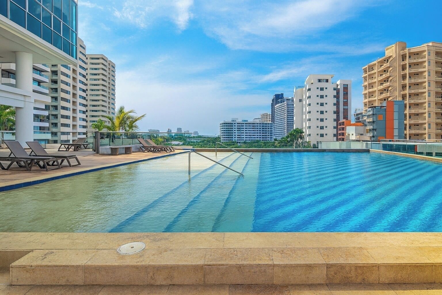 A rooftop pool with lounge chairs and a view of surrounding high-rise buildings.