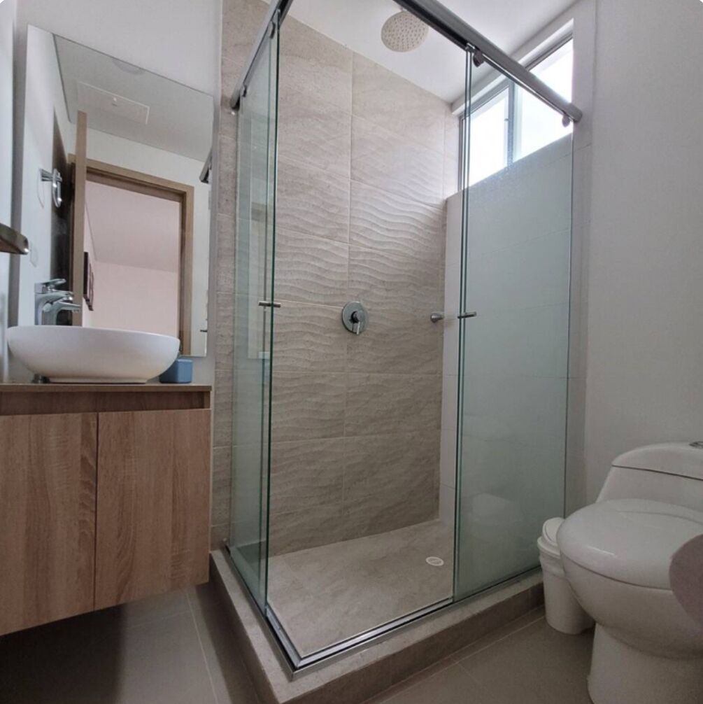 Une salle de bain moderne avec une douche à parois de verre, un meuble-lavabo en bois et des toilettes blanches.