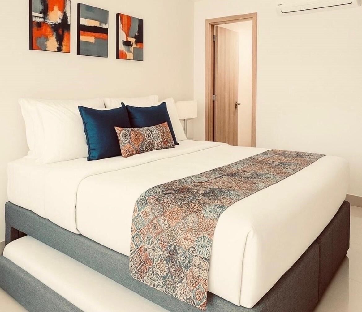 A modern bedroom with a large bed, a bench at the foot, and abstract art on the wall.