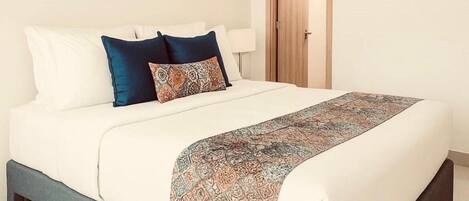 A modern bedroom with a large bed, a bench at the foot, and abstract art on the wall.