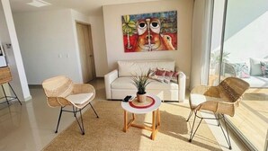 Una sala de estar moderna con un sofá, dos sillones de mimbre, una mesita de centro y un cuadro abstracto grande en la pared.