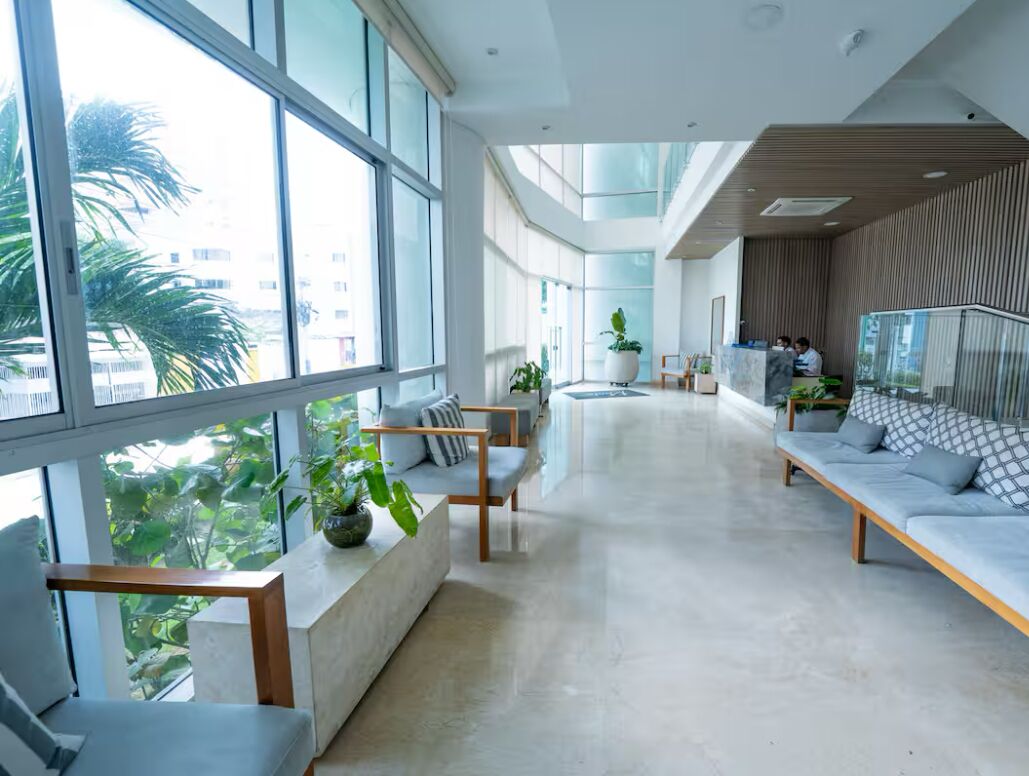 Un vestíbulo amplio con ventanas grandes, zonas de estar y plantas de interior.