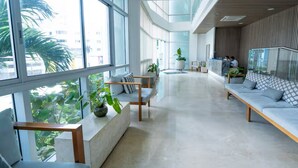 Un vestíbulo amplio con ventanas grandes, zonas de estar y plantas de interior.