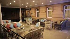 A well-lit indoor seating area with wicker furniture and a glass table, featuring a balcony with a railing. - Hotel BEK Tashkent (Tashkent)