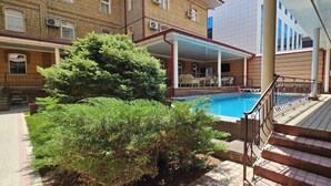 A hotel with a swimming pool, outdoor seating, and a covered patio area. - Hotel BEK Tashkent (Tashkent)