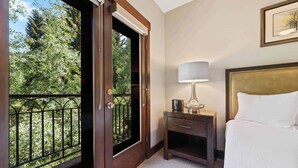 A hotel room with a bed, a nightstand with a lamp, a door leading to a balcony with a view of trees. - The Charter at Beaver Creek C2305 - Mountain Living (Beaver Creek)