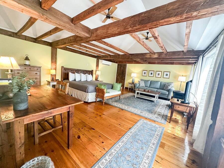 Un'ampia stanza con travi in legno, un letto, una divano, un tavolo da pranzo e una televisione.