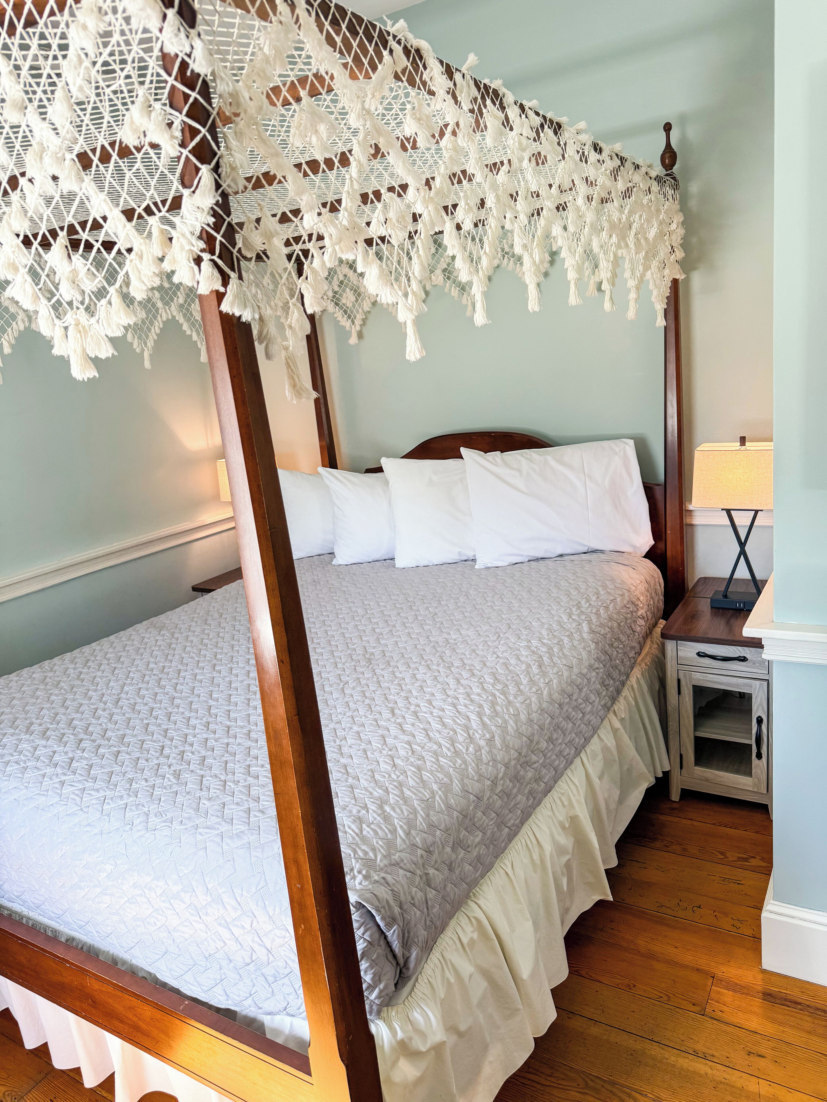 A four-poster bed with a white canopy, a wooden headboard, and a bedside table with a lamp.
