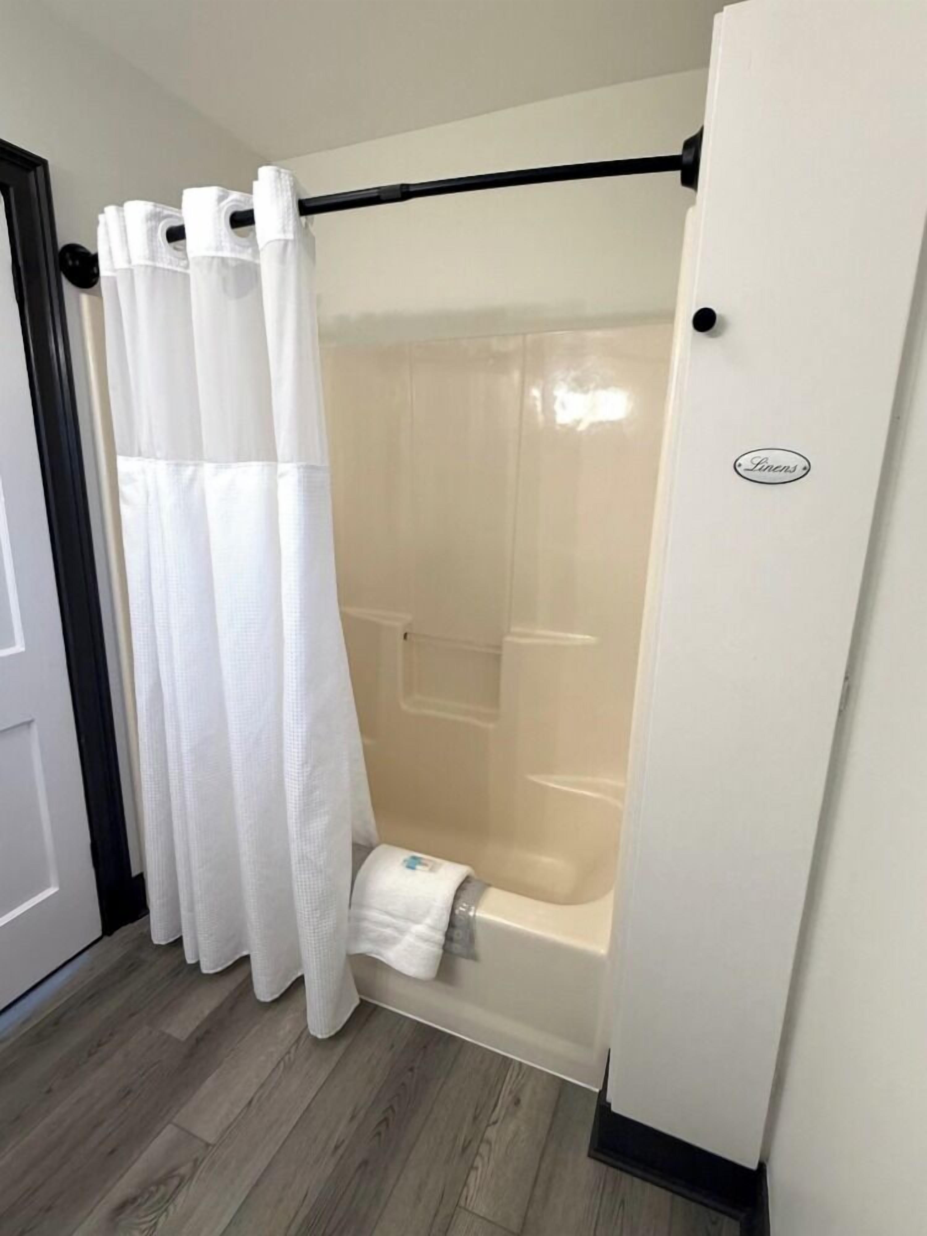 Un área de ducha con una cortina blanca, una toalla y una bañera.